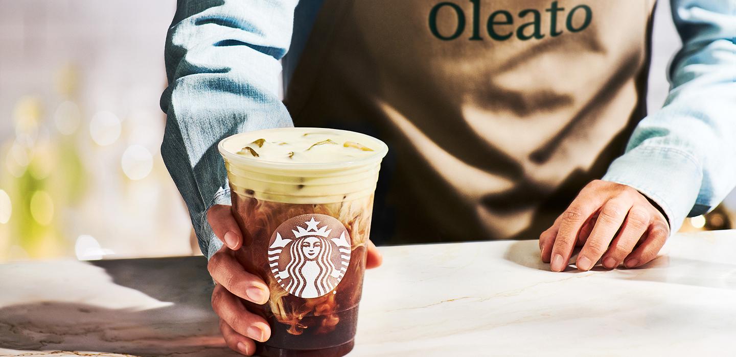 「Oleato」と呼ばれる茶色のエプロンを着たバリスタが、スターバックスの Oleato Golden Foam Cold Brew を手渡します。